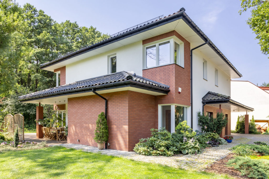 Red brick house with terrace and green grass and trees during su